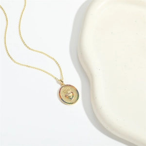 Golden oval cross necklace with heart and colored zircon on a minimalist white backdrop