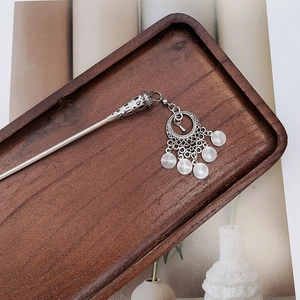 Detailed close-up of antique silver tassel hairpin on dark wooden tray in vintage style