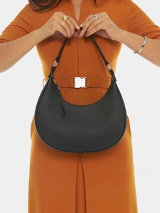 Detail of a black leather crescent hobo bag with silver buckle held by a model