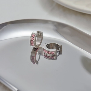 Close-up of silver earrings with pink zircon stones on a reflective metal tray