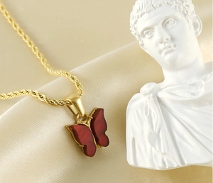 Detailed macro view of a red butterfly pendant on a golden rope chain over silk