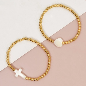 Detailed shot of handmade beaded gold bracelets with heart and cross mother of pearl charms