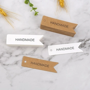 Detail of swallowtail handmade paper tags in brown kraft and white on marble surface