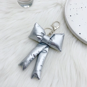 Silver padded metallic bow keychain on white faux fur background for bag accessory