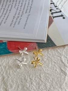 Detailed view of irregular bow stud earrings in polished gold and silver metal finishes