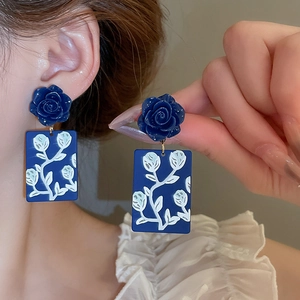 Detail of blue resin rose earrings with floral painted charms worn on the earlobe