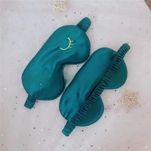 Detail of dark green silk sleep mask with embroidered eyelashes and elastic strap