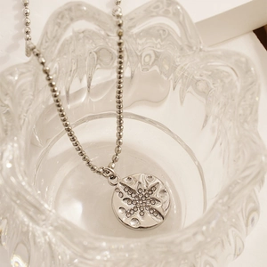 Silver starburst pendant necklace with rhinestones and bead chain in a glass bowl