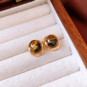 Macro shot of 18k gold plated tiger eye stone earrings on white velvet jewelry box