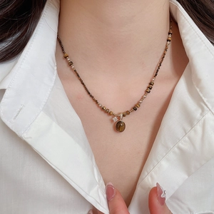 Close-up of beaded tiger eye necklace with gold oval pendant worn on a white shirt