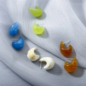 Close-up of resin stud earrings in lime, navy, and marble on blue silk fabric