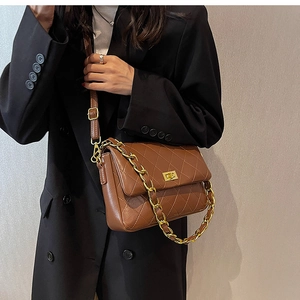 Close-up of brown quilted crossbody bag with gold chain strap on black blazer