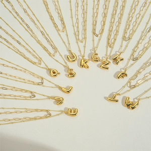 Golden double-layer initial pendant necklace featuring bold letter charms on beige surface