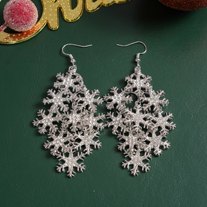 Silver snowflake drop earrings with sparkling crystals on a dark green surface