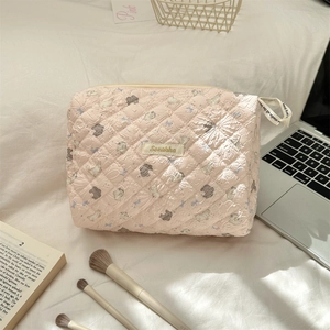 Pink quilted floral makeup bag with bunny pattern on white bedding with accessories
