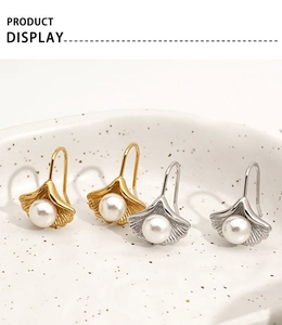 Macro detail of ginkgo leaf earrings with pearls in gold and silver finish on ceramic tray