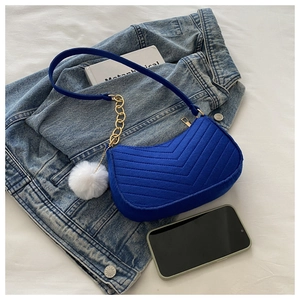Detalle del bolso de hombro en ante azul real con acolchado en V y un suave pompón blanco