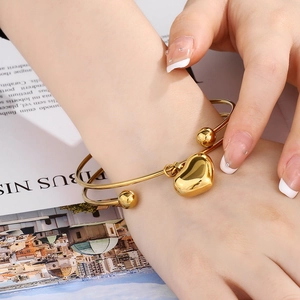 Close-up of 18K gold plated heart charm bangle on wrist with aesthetic background
