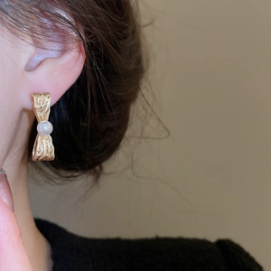Dettaglio dell'orecchino a fiocco dorato con perla bianca indossato su orecchio