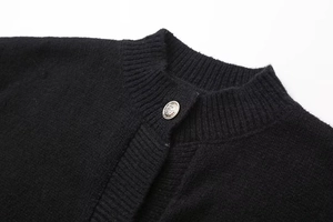 Gros plan d'un gilet en maille noire avec bouton métallique argenté sculpté sur le col