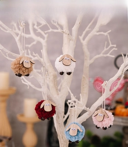 Detail of colorful plush and wood sheep ornaments hanging from a decorative white branch