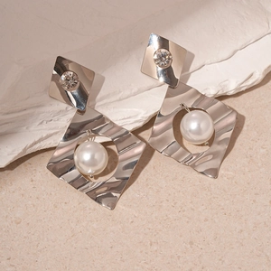Detailed view of silver geometric earrings with sparkling crystals and large white pearls
