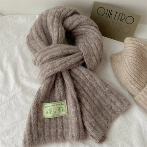 Close-up of oatmeal knit scarf texture showing wool label and ribbed pattern detail