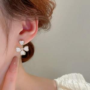 Détail de boucles d'oreilles dorées avec pétales blancs en cœur et diamant sur un mannequin