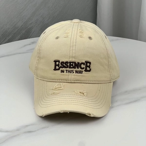 Detail of distressed beige cotton baseball cap with embroidered letters and torn edges