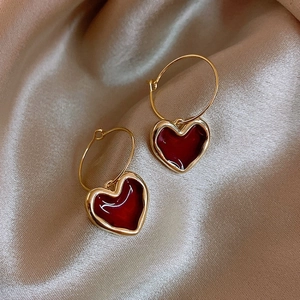 Elegant gold hoop earrings with burgundy heart pendants on a champagne satin background