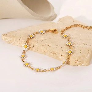 Detalle de una pulsera de margaritas doradas con esmalte blanco sobre una piedra beige