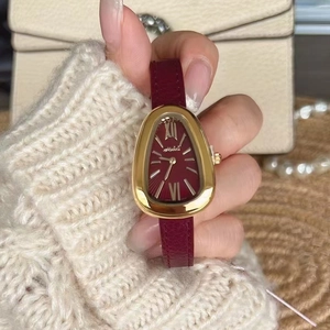 Detail of luxury snake-head gold watch case with deep red dial and leather strap