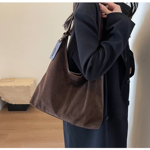 Detail of a large brown suede hobo bag with metal buckle worn with a black wool coat