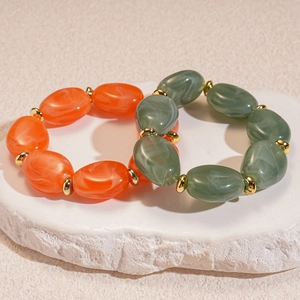 Detail of irregular acrylic oval beads in orange and grey with gold spacers on stone