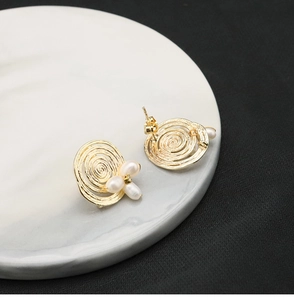 Macro detail of golden spiral stud earrings with white pearl accents on marble