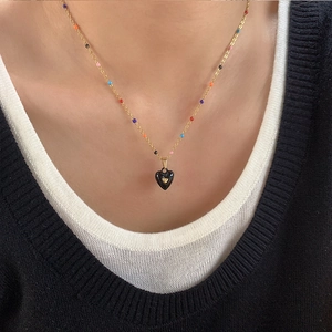 Macro detail of gold necklace with black heart pendant and colorful enamel beads