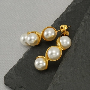 Detail of gold twisted hoop earrings with three white pearls on a grey stone texture