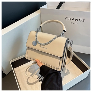Detail of beige faux leather handbag with silver chain and logo tag in a gift box