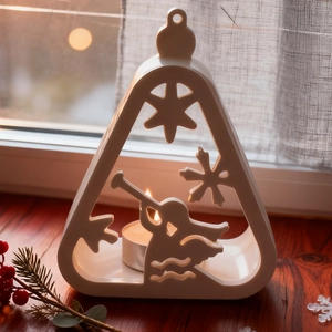 Close-up of white ceramic hollow candle holder with angel motifs and warm candlelight