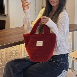 Detail of red plush tote bag featuring a white textile label in a cozy cafe setting