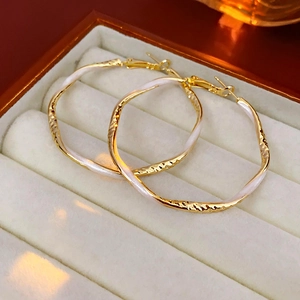 Macro detail of gold-tone metal earrings with white enamel on a soft velvet box