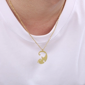 Détail d'un collier pendentif silhouette de chat doré porté sur un t-shirt blanc propre