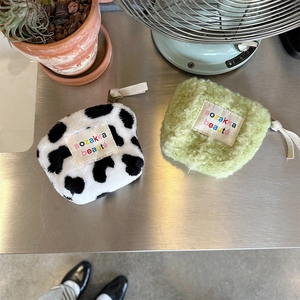 Detail of plush mini makeup bags in cow print and green with embroidered fabric labels