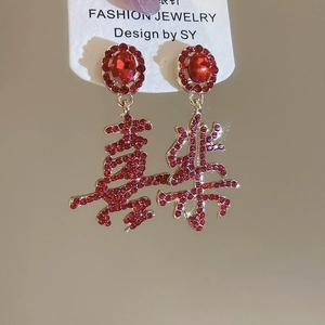 Close-up of red Chinese New Year earrings with 'Xile' characters in gold and red gems