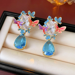 Detailed close-up of vintage gold earrings with colorful enamel butterflies and blue teardrop stones