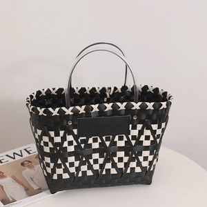 Handwoven checkerboard straw basket bag with transparent round handles on a white table