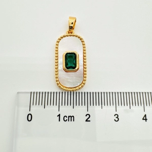 Macro detail of a 18K gold plated rectangle pendant with green gem and shell inlay next to a ruler