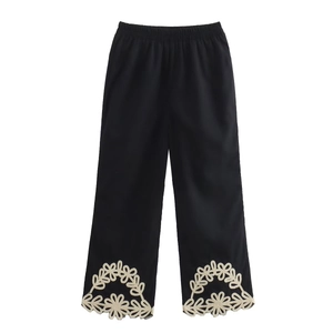 Gros plan détaillé du pantalon noir avec broderie florale blanche sur l'ourlet
