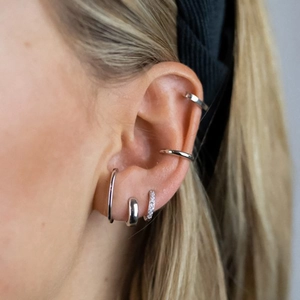 Close-up of silver hoop earrings and ear cuffs with micro-set cubic zirconia on ear