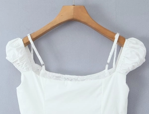 Detail of white top showing lace neckline, delicate spaghetti straps and puffy sleeves